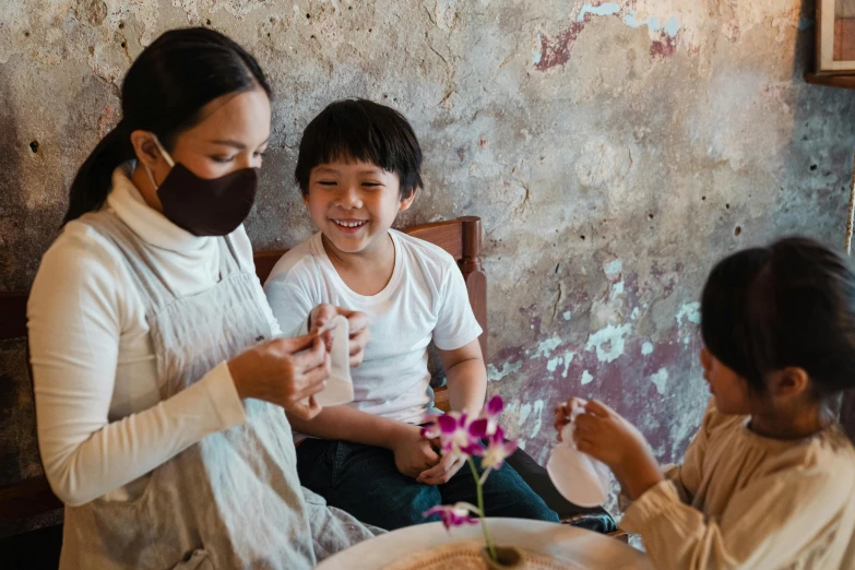 a woman and two children sitting at a table, pexels contest winner, flower mask, bao phan, manuka, fully functional