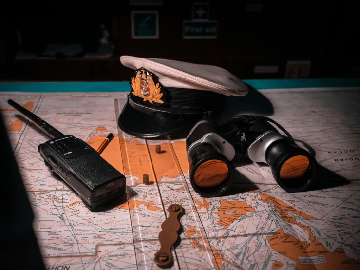 a hat sitting on top of a map next to a pair of binoculars, a colorized photo, unsplash, photorealism, officers uniform, board games on a table, sunken, raytracing on