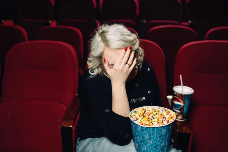 a woman sitting in front of a bucket of popcorn, by Julia Pishtar, pexels contest winner, she's sad, sydney sweeney, in a cinema, amanda lilleston