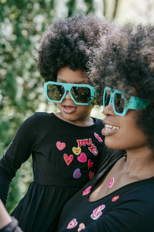 a woman taking a picture of a little girl wearing sunglasses, funk art, natural hair, teal, hearts, 40 years old women