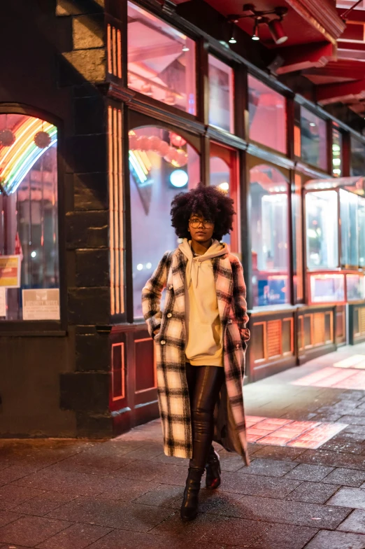 a woman walking down a city street at night, a portrait, trending on unsplash, tartan hoodie, outside a saloon, long afro hair, long coat