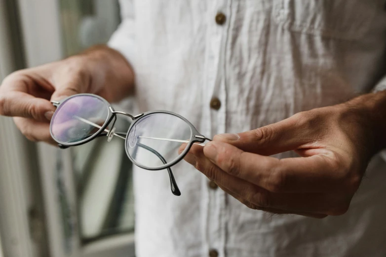 a close up of a person holding a pair of glasses, silver monocle, natural soft rim light, iridescent titanium, round glasses potter