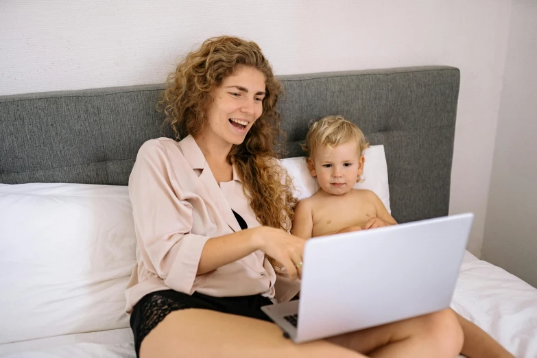 a woman sitting on a bed with a baby on her lap, a cartoon, pexels, coding time, a blond, 1x, everyone having fun