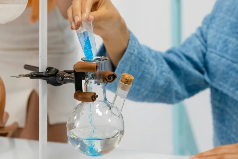 a close up of a person holding a beaker filled with liquid, trending on pexels, with pipes attached to it, perfume, blue, avatar image