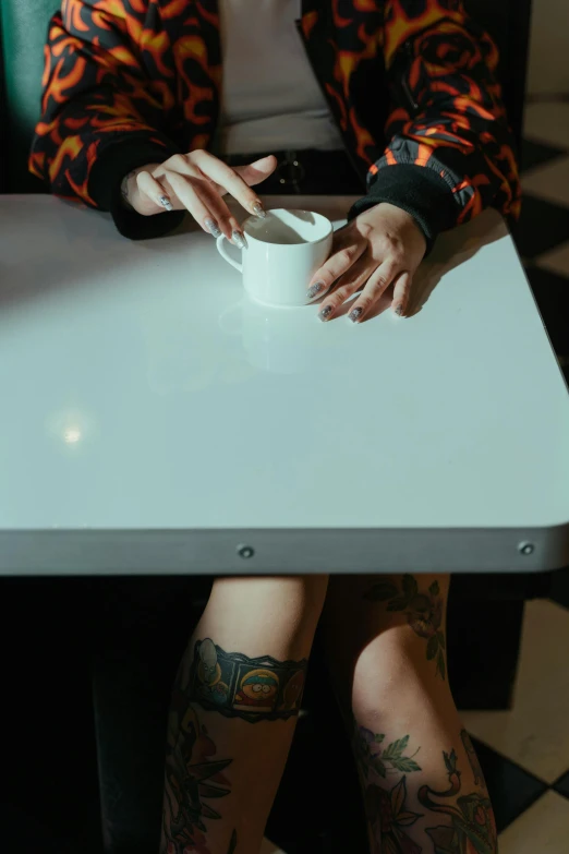 a woman sitting at a table with a cup of coffee, a tattoo, trending on pexels, hyperrealism, low quality photo, 35 mm photo