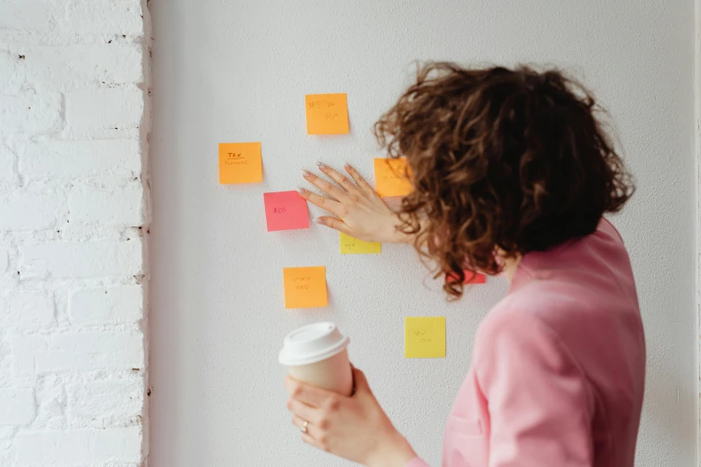 a woman standing in front of a wall covered in post it notes, trending on pexels, next to a cup, pink and orange colors, inspect in inventory image, product image