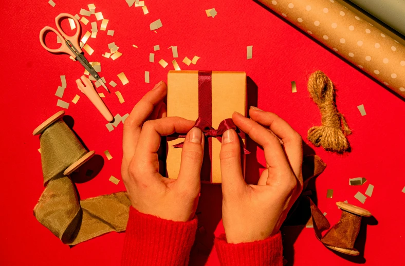 a person holding a gift wrapped in brown paper, by Julia Pishtar, pexels contest winner, process art, on a red background, background image, santa's workshop, opening shot