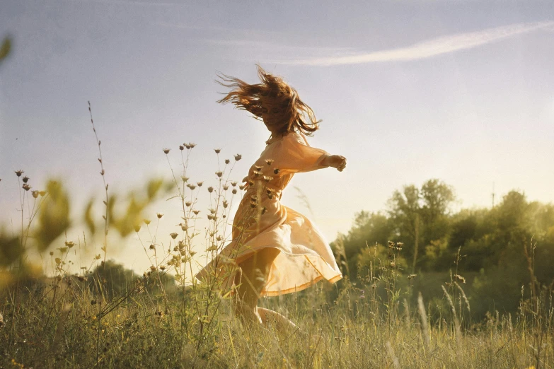 a woman in a yellow dress running through a field, an album cover, by Pamela Ascherson, pexels contest winner, figuration libre, flowing backlit hair, sadie sink, excitement, early morning light