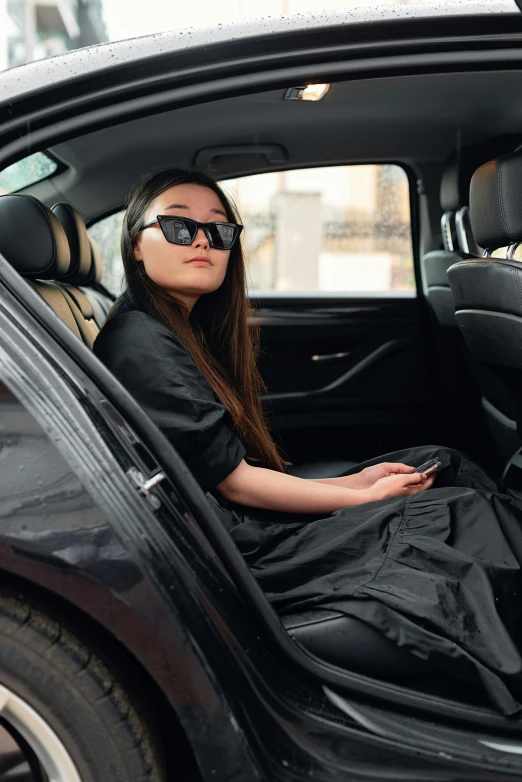 a woman sitting in the back seat of a car, vantablack cloth technology, square, wearing a robe, tardigrade wearing sunglasses