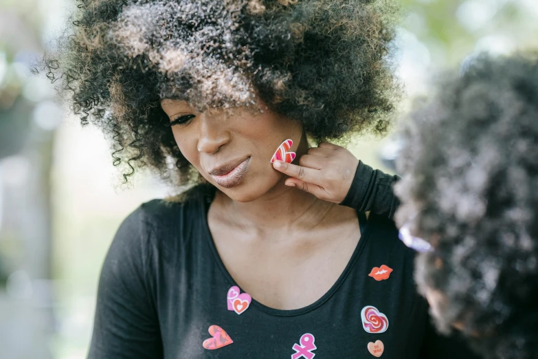 a woman putting lipstick on another woman's lips, by Lily Delissa Joseph, trending on pexels, curly afro, wearing jewellery, hearts, sza