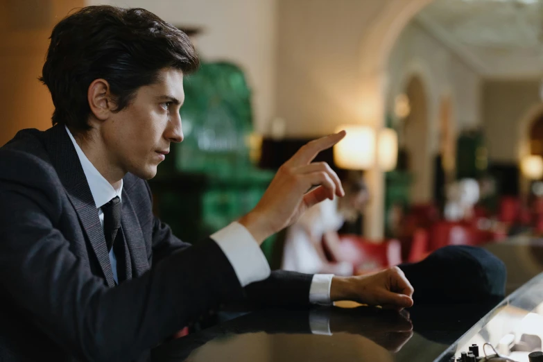 a man in a suit sitting at a bar using a cell phone, trending on pexels, visual art, adam driver, pointing, f 1 driver charles leclerc, in front of a computer