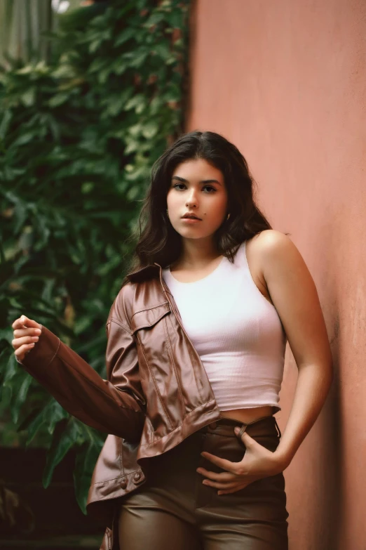 a woman standing in front of a pink wall, an album cover, by Robbie Trevino, trending on pexels, renaissance, wearing brown leather jacket, madison beer girl portrait, grainy, brown:-2