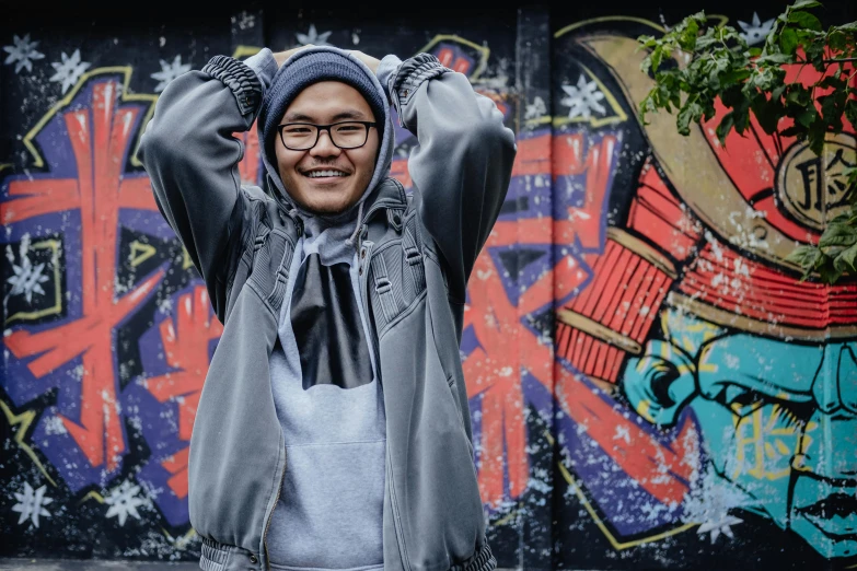 a man standing in front of a graffiti covered wall, a portrait, inspired by Gang Hui-an, pexels contest winner, wearing a grey hooded sweatshirt, playful smile, avatar image, jesper esjing