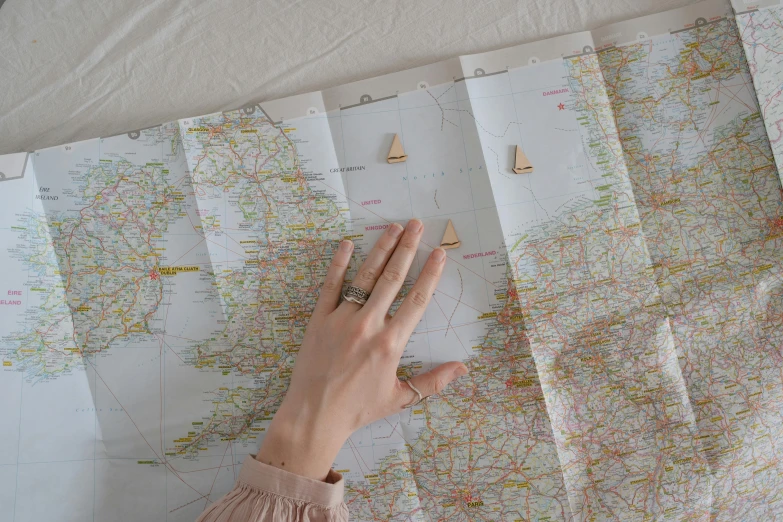 a person holding a piece of paper on top of a map, by Helen Stevenson, trending on unsplash, visual art, rings, wooden sailboats, pink, uk