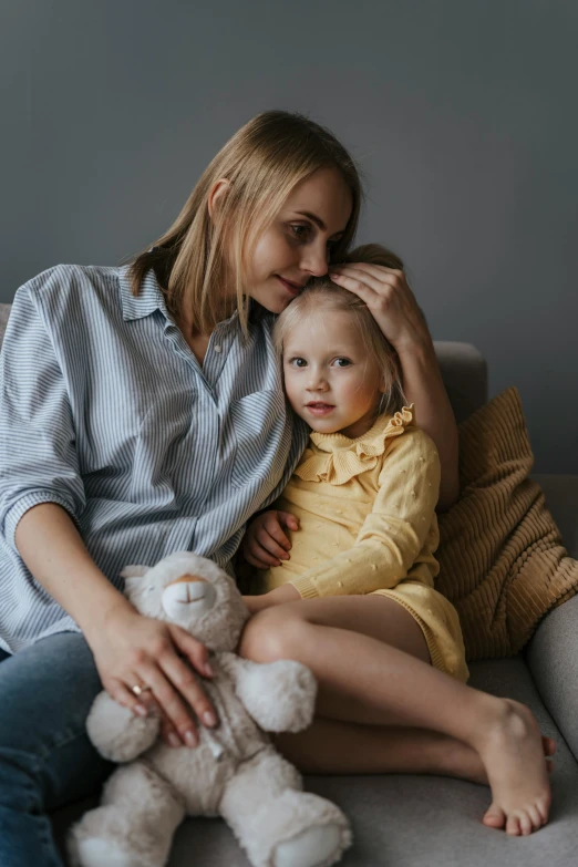a woman sitting on a couch holding a small child, pexels, soft hair, on a gray background, goldilocks, thumbnail