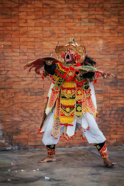 a man in a costume standing in front of a brick wall, pexels contest winner, happening, bali, square, strong and ferocious, dressed in ornate