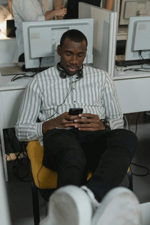 a man sitting in a chair looking at his cell phone, trending on pexels, happening, in an call centre office, kano), who is a male android, professional sports style