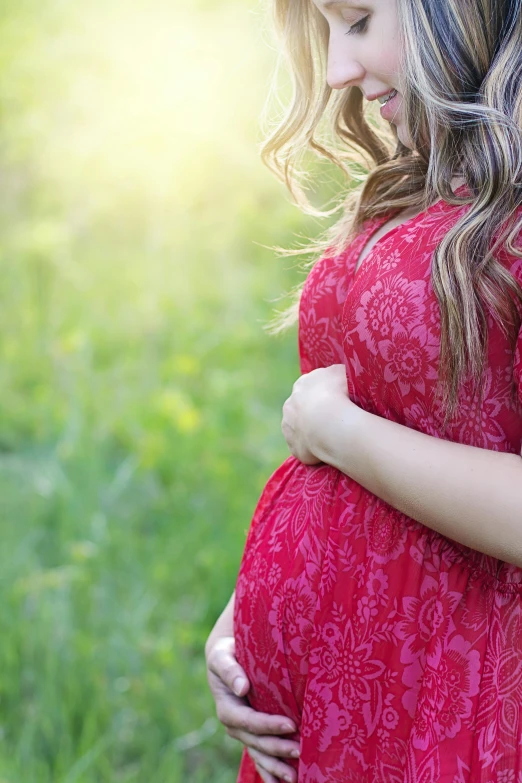 a pregnant woman in a red dress standing in a field, hugging and cradling, profile image, rectangle, sunshine