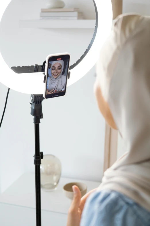 a woman taking a picture of herself in a mirror, hurufiyya, ring light, live broadcast, modest, studio gibli