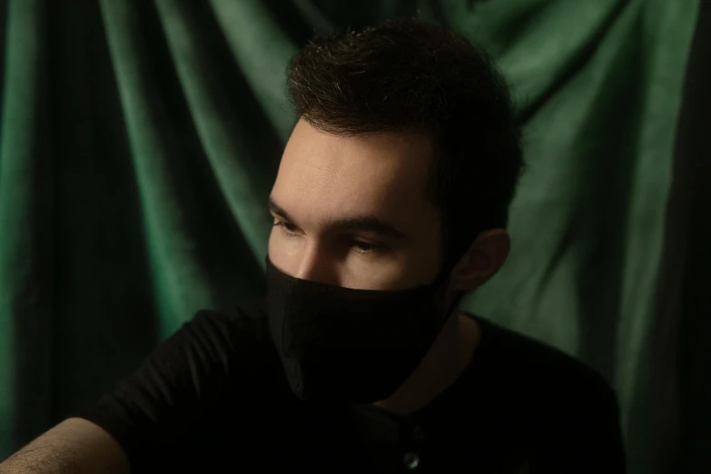 a man with a black face covering his mouth, an album cover, by Adam Marczyński, pexels contest winner, realism, gradient from green to black, he is wearing a black t-shirt, youtube video screenshot, julian ope