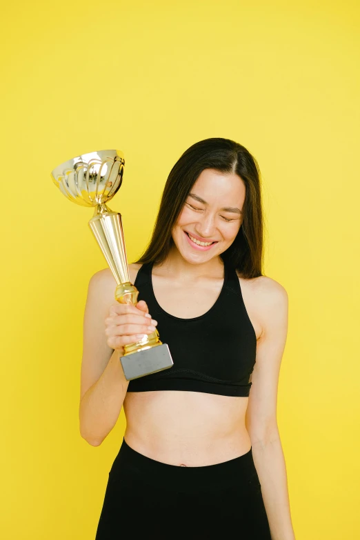 a woman in a sports bra top holding a trophy, pexels contest winner, on a yellow canva, young asian woman, heavily upvoted, tall