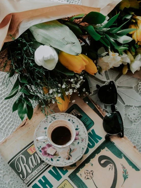 a bouquet of flowers sitting on top of a table next to a cup of coffee, by Lucia Peka, trending on unsplash, vintage photo, multiple stories, detailed product image, flowers covering eyes