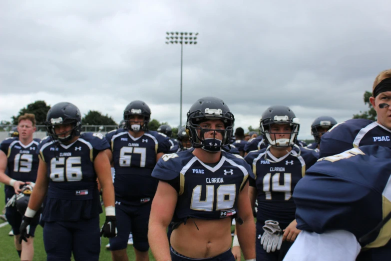 a group of football players standing on top of a field, liam brazier, navy, helmet, female looking