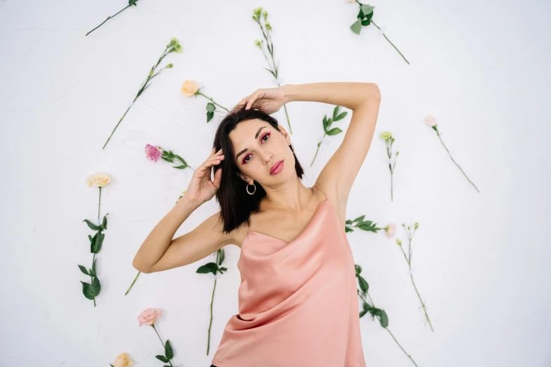 a woman posing in front of a wall with flowers, trending on pexels, aestheticism, flowing salmon-colored silk, dua lipa, in front of white back drop, wearing a camisole