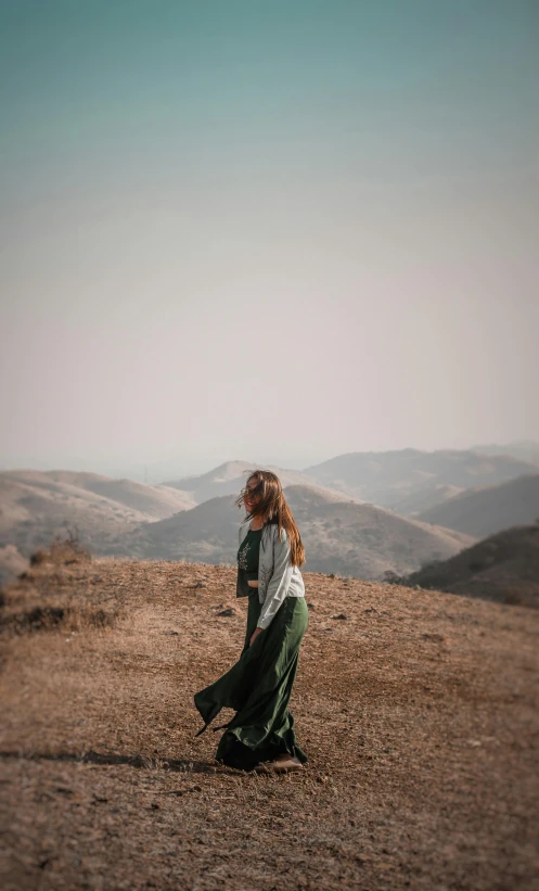 a woman standing on top of a dirt field, by Matt Cavotta, pexels contest winner, white shirt and green skirt, over the hills, 15081959 21121991 01012000 4k, wearing a long dress