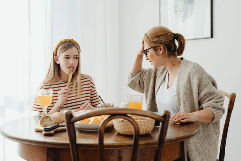 two women sitting at a table having breakfast, by Julia Pishtar, trending on pexels, caring fatherly wide forehead, arguing, teenage no, sitting on top a table
