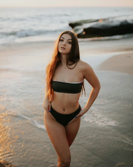 a woman standing on top of a beach next to the ocean, by Robbie Trevino, in a black betch bra, pale glowing skin, portrait featured on unsplash, cute girl wearing tank suit