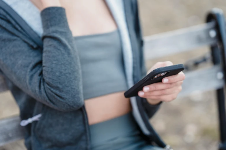 a woman sitting on a bench holding a cell phone, trending on pexels, jacket over bare torso, two piece workout clothes, zoomed in, your personal data avatar