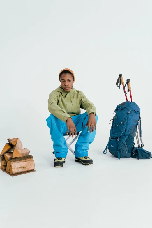 a man sitting next to a pile of wood and a backpack, inspired by Barthélemy Menn, teal suit, high elevation, wearing a hoodie and sweatpants, jayison devadas