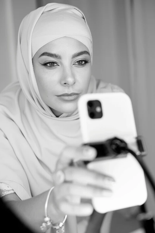 a woman taking a picture of herself in a mirror, a black and white photo, inspired by Maryam Hashemi, hurufiyya, holds a smart phone in one hand, arab ameera al-taweel, portrait of sofia vergara, ((portrait))