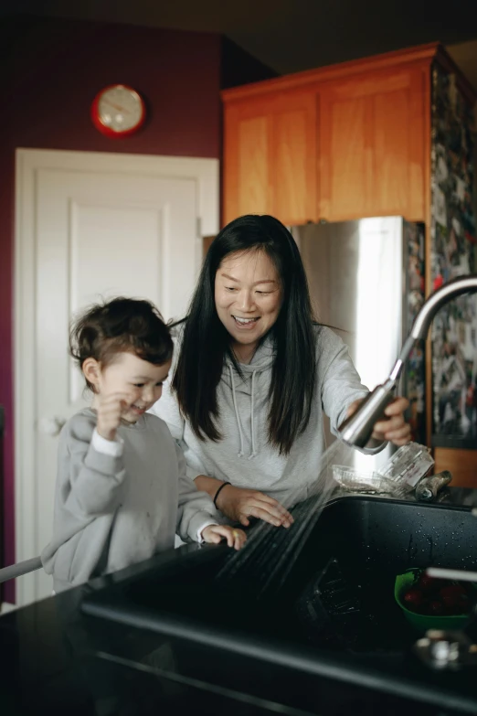 a woman and a child washing their hands in a kitchen sink, inspired by Li Di, happening, half asian, programming, high-quality photo, laughing