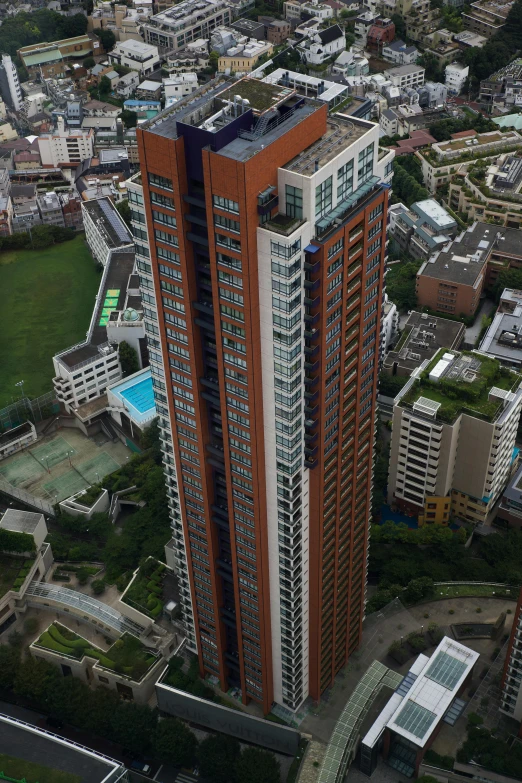 a tall building sitting on top of a lush green field, in hong kong, birds - eye view, red building, bo chen