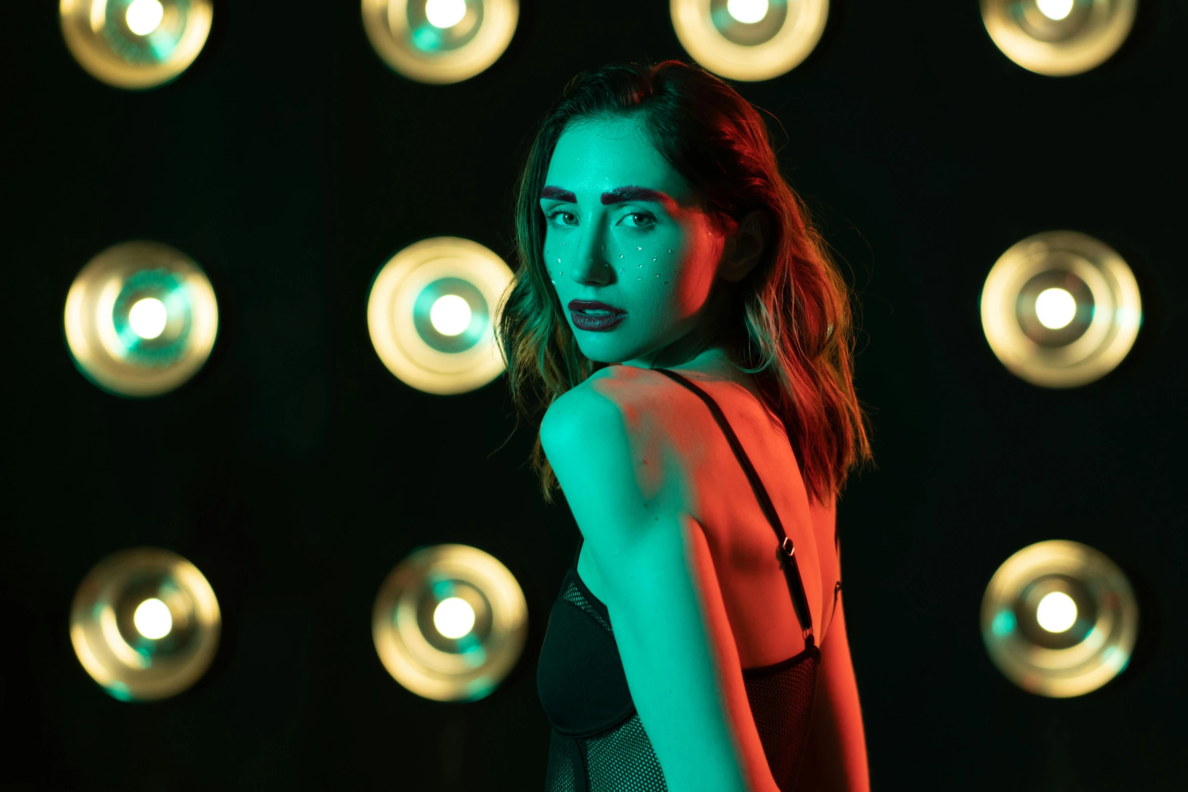 a woman standing in front of a wall of lights, inspired by Elsa Bleda, pexels contest winner, green body. red eyes, lilly collins, ( ( stage lights ) ), non binary model