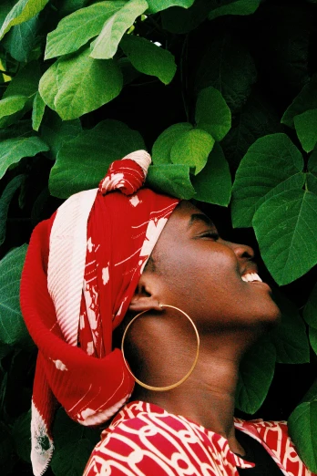 a woman wearing a red and white scarf and gold hoop earrings, an album cover, inspired by Ras Akyem, trending on pexels, lush greenery, hat covering eyes, ( ( dark skin ) ), analogue photo
