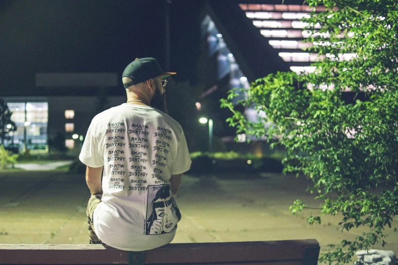 a man sitting on top of a wooden bench, a portrait, by Bascove, unsplash, graffiti, graphic tees, from the back, summer night, detailed white