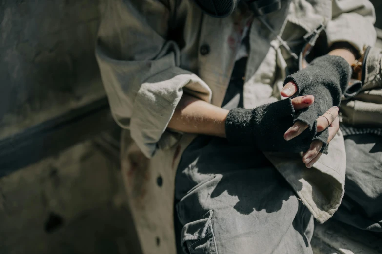 a close up of a person holding a glove, by Emma Andijewska, trending on unsplash, arte povera, post apocalyptic scene, black bandage on arms, sitting on the ground, japanese live-action movie