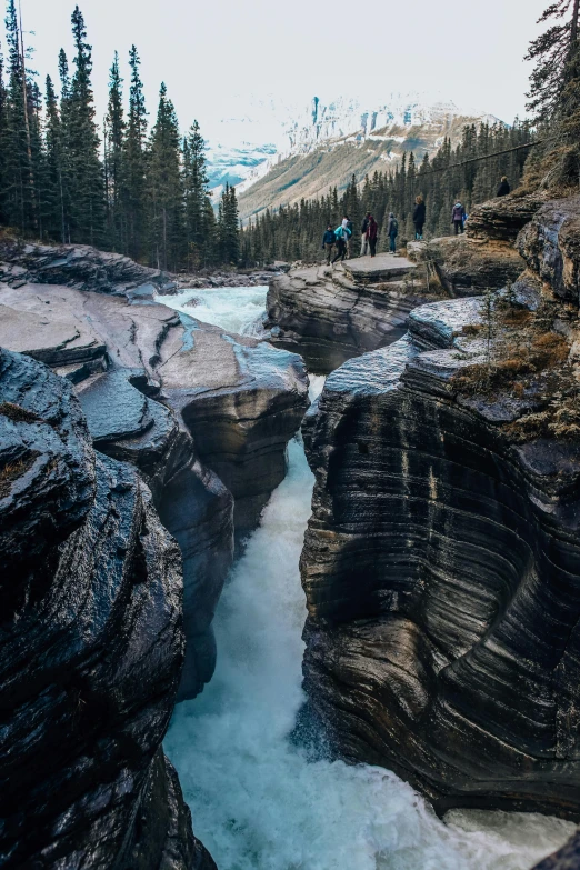 a group of people standing on top of a mountain next to a river, inspired by James Pittendrigh MacGillivray, pexels contest winner, erosion channels river, canada, marble hole, rapids
