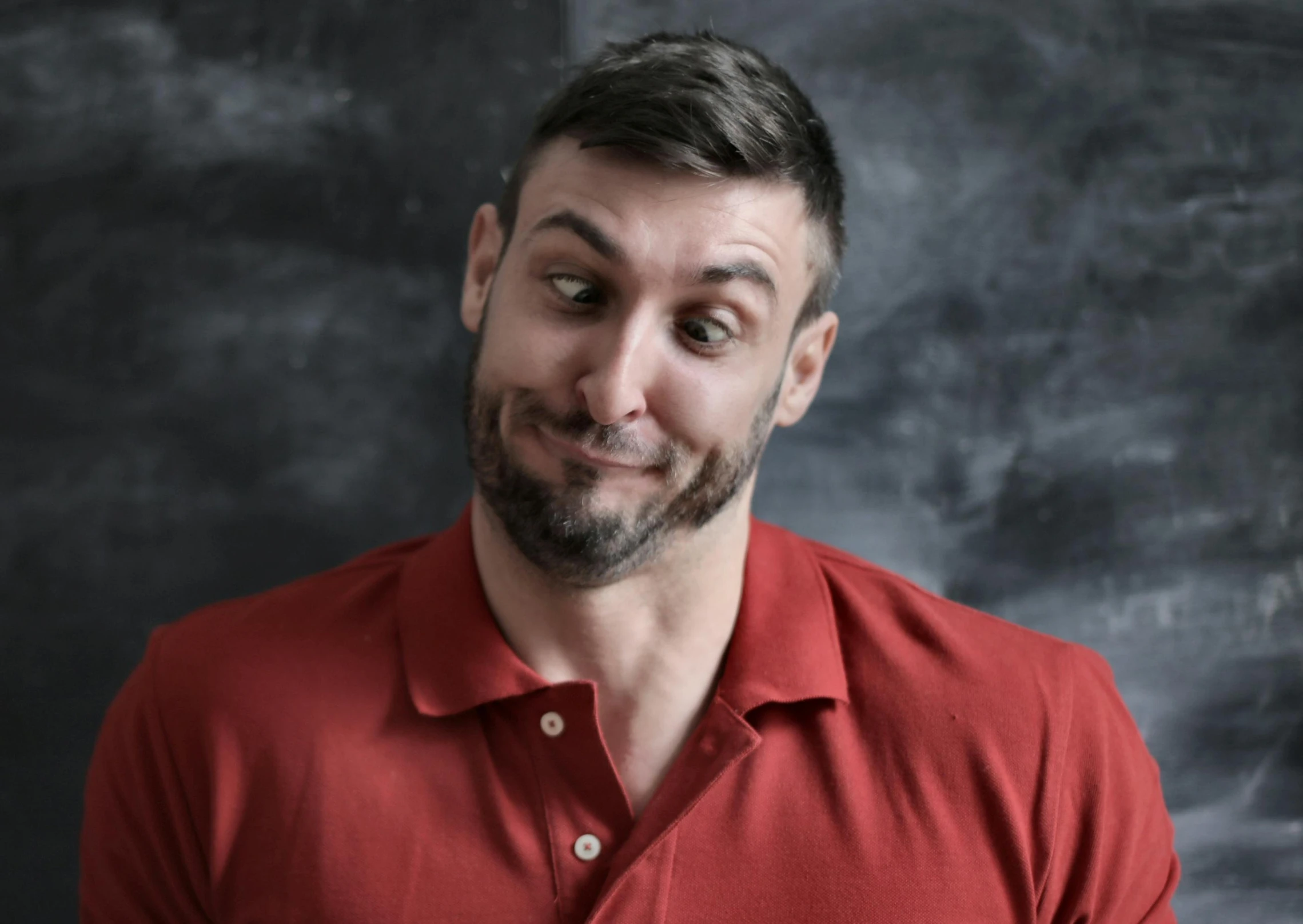 a man in a red shirt standing in front of a blackboard, a portrait, pexels contest winner, round teeth and goofy face, stjepan sejic, on grey background, uncomfortable crooked smile