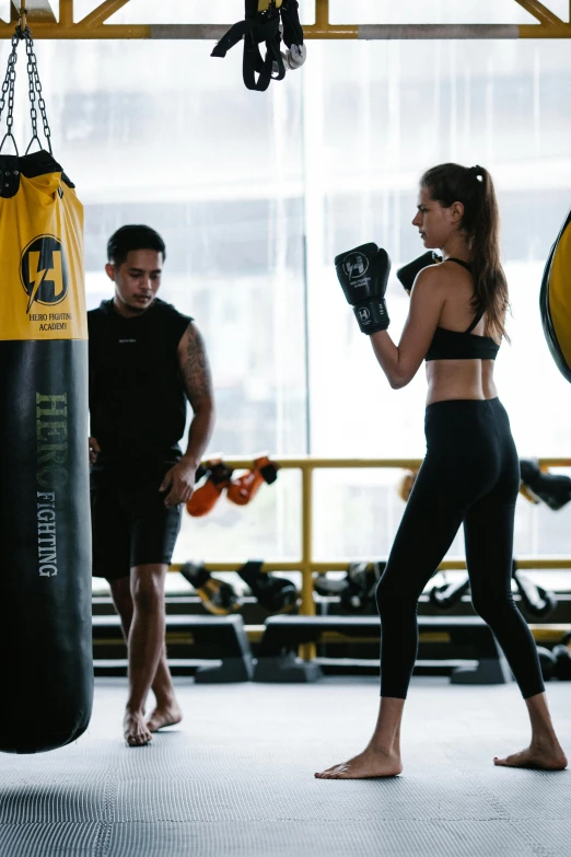 a group of people in a gym with punching bags, by Niko Henrichon, happening, yellow and black color scheme, bangkok, hero, thumbnail