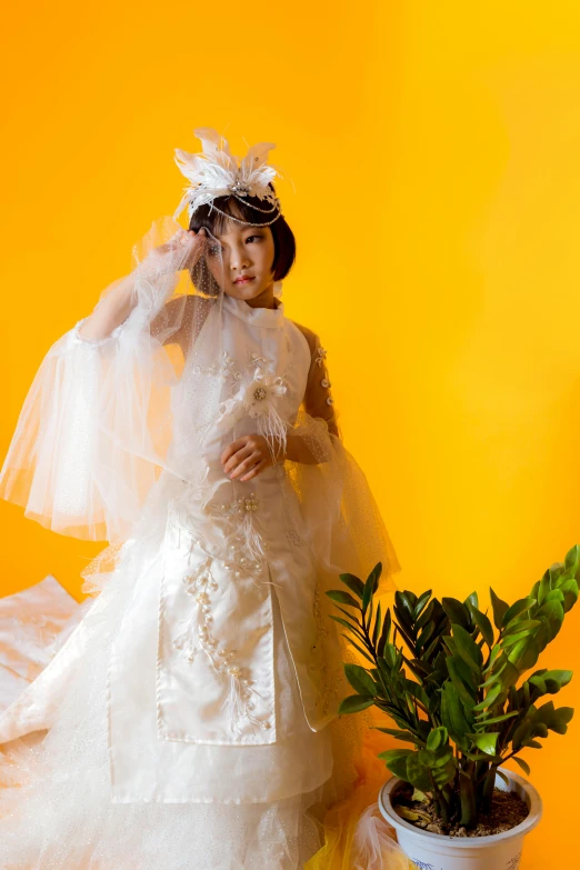 a woman in a wedding dress standing next to a potted plant, inspired by Cecil Beaton, unsplash, rococo, angelic pretty, in front of an orange background, paru itagaki, wings lace wear