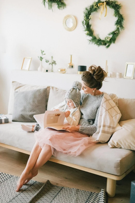 a woman sitting on a couch reading a book, a picture, pexels contest winner, maternity feeling, holding gift, pink and grey muted colors, daughter