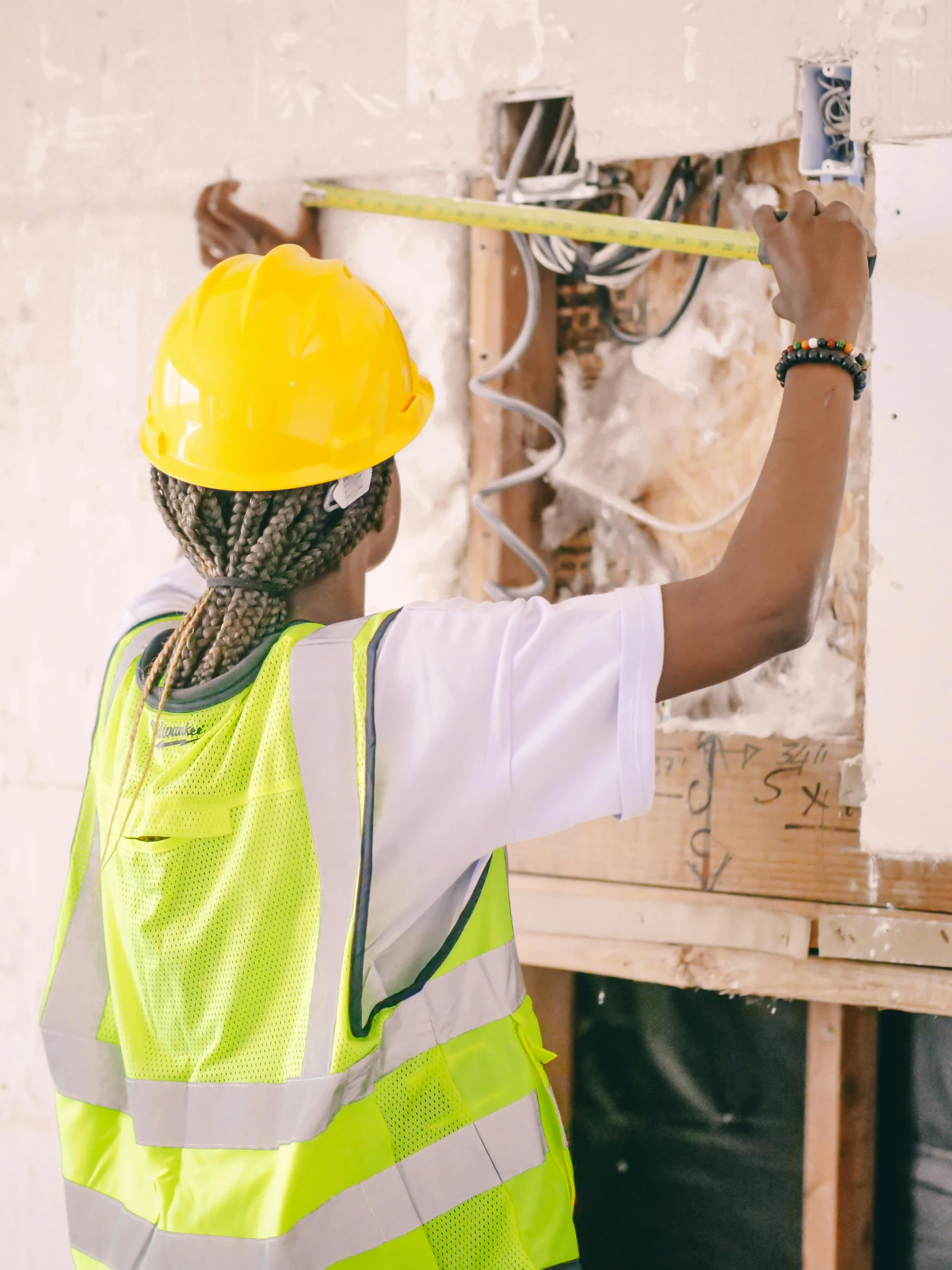 a woman in a hard hat working on a wall, inspired by Afewerk Tekle, pexels contest winner, electrical details, promo image, people looking at a house, wearing hi vis clothing