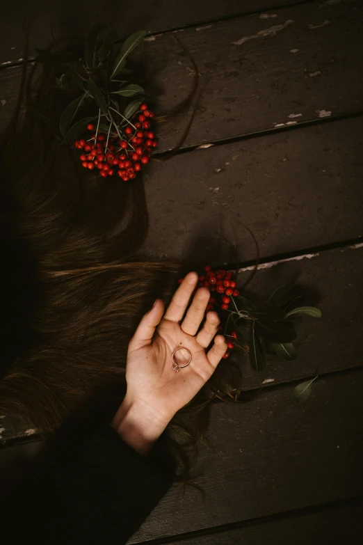 a woman with long brown hair laying on a wooden floor, inspired by Elsa Bleda, pexels contest winner, symbolism, berries, hand, ignant, holiday season