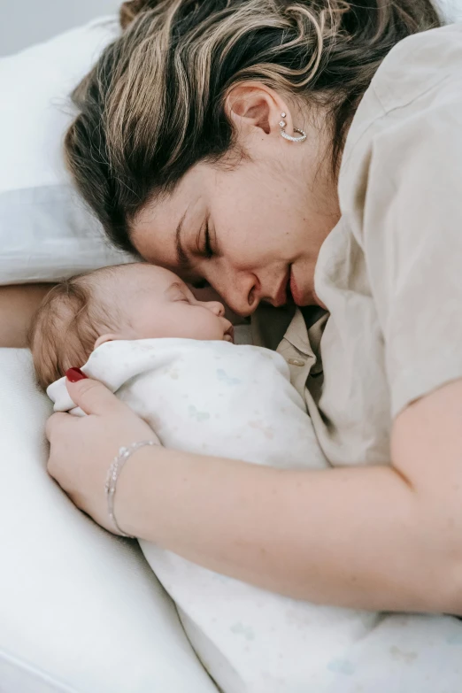 a woman laying in bed with a baby, pexels contest winner, symbolism, hugging each other, profile image, angled shot, small