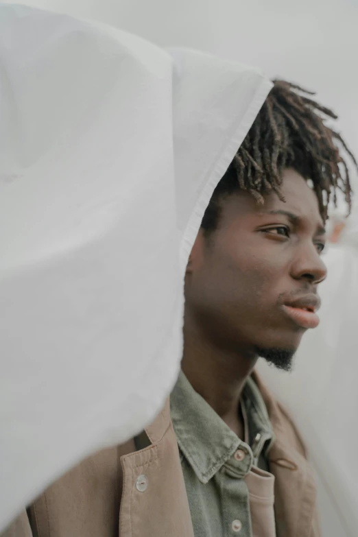 a man with dreadlocks standing under a white sheet, trending on unsplash, with brown skin, looking away, a young man, overcast day