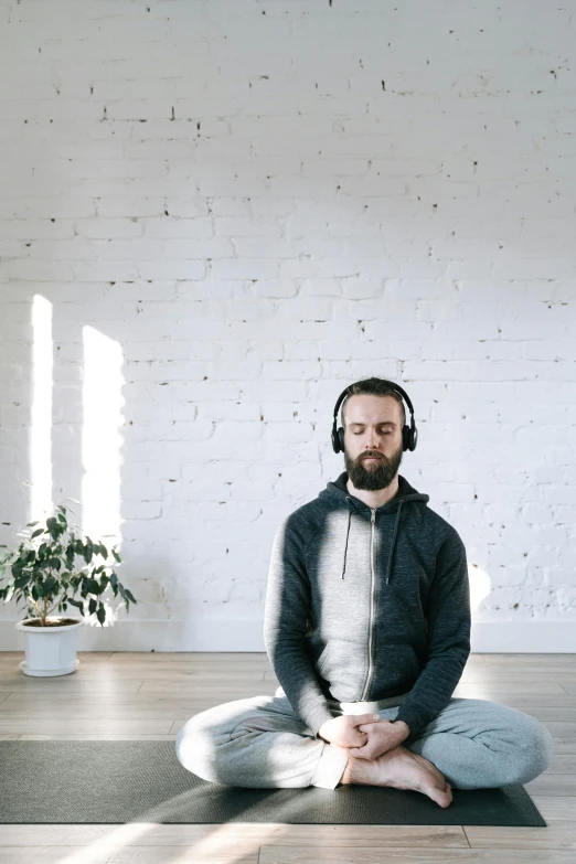 a man sitting on a yoga mat with headphones on, trending on pexels, light and space, head is centered, low quality photo, digital oth, in a room